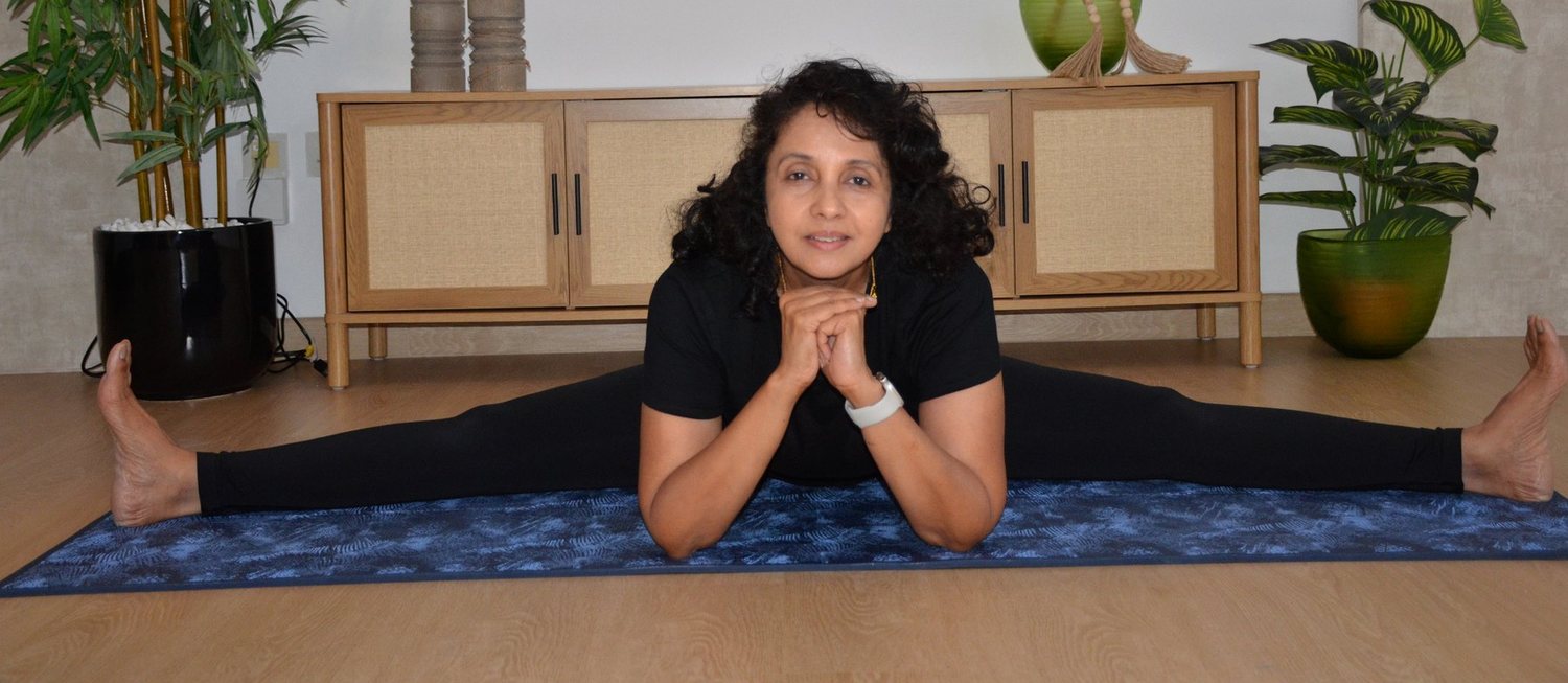 Shipra in a full seated straddle, forearms resting on the mat